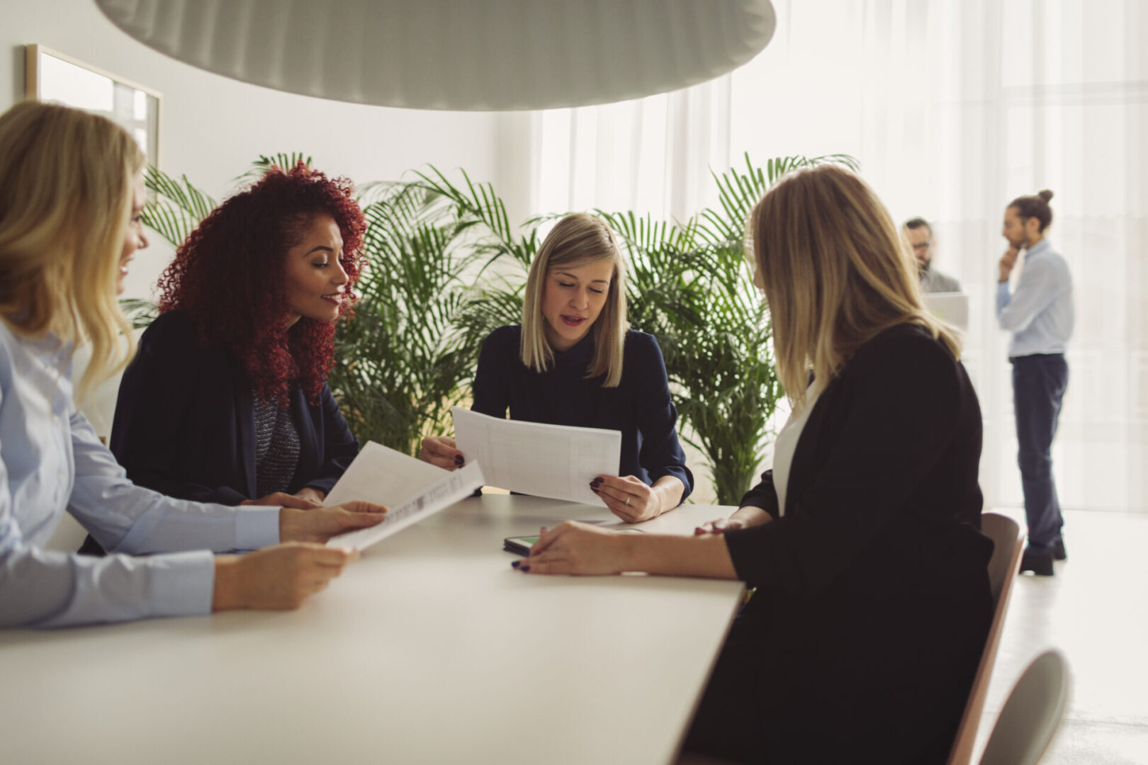 Businesswomen Working Together In The Moder Office. Sitting by the desk on meeting, discussing and looking papers with digital tablet in front of them.